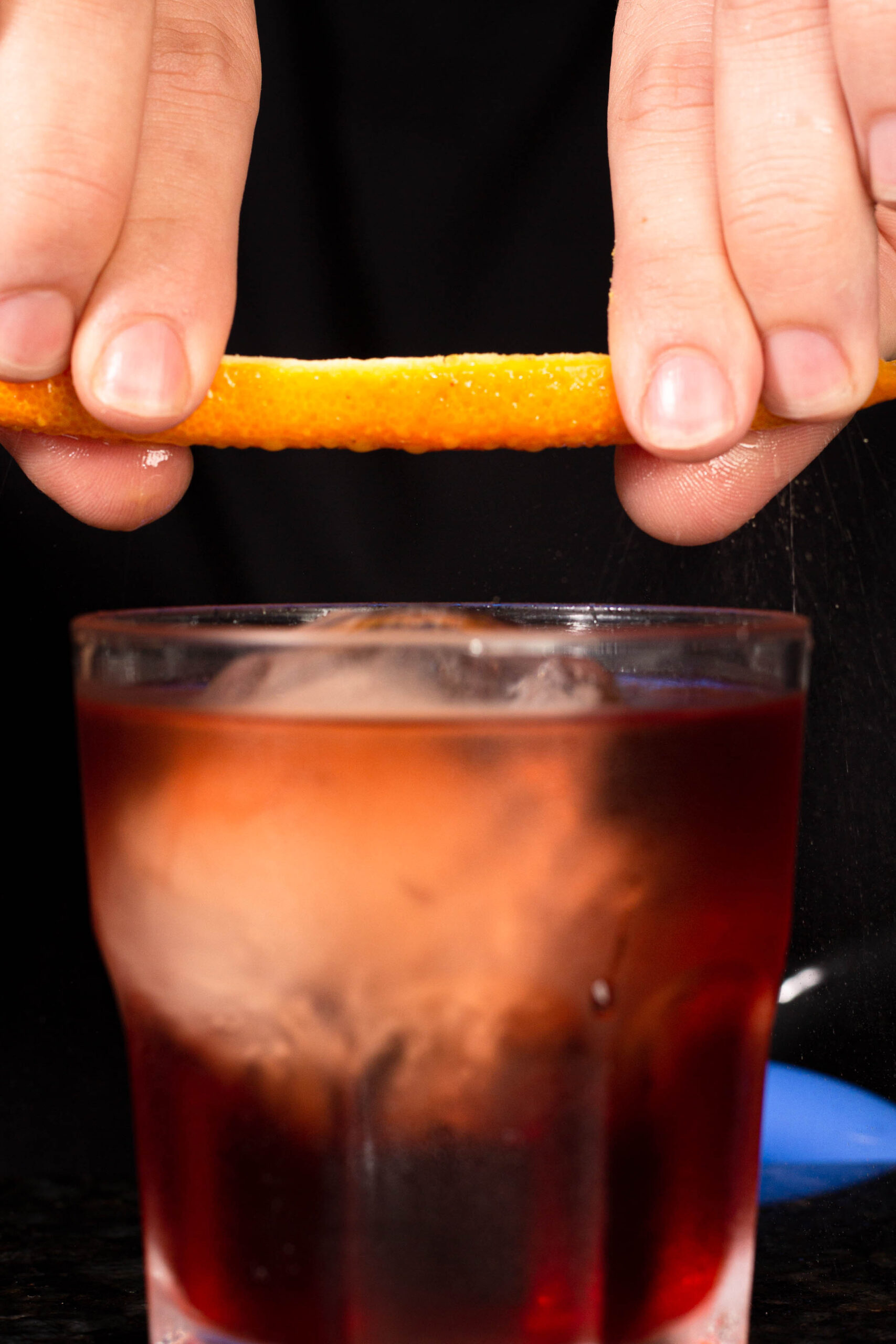 mão espremendo casca de laranja em um copo com drink.