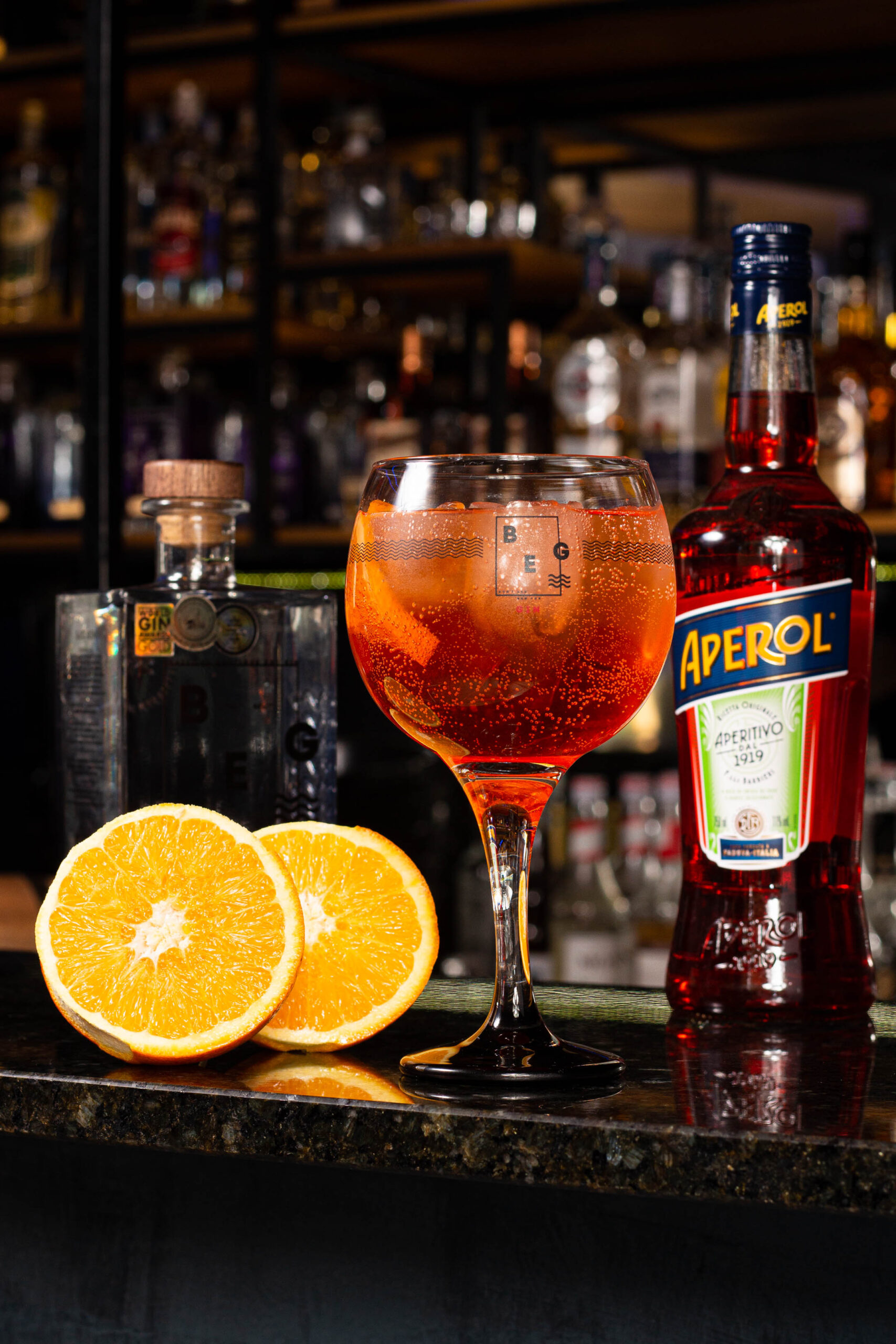 copo de drink ao seu lado duas garrafas de bebida e uma laranja fatiada ao meio