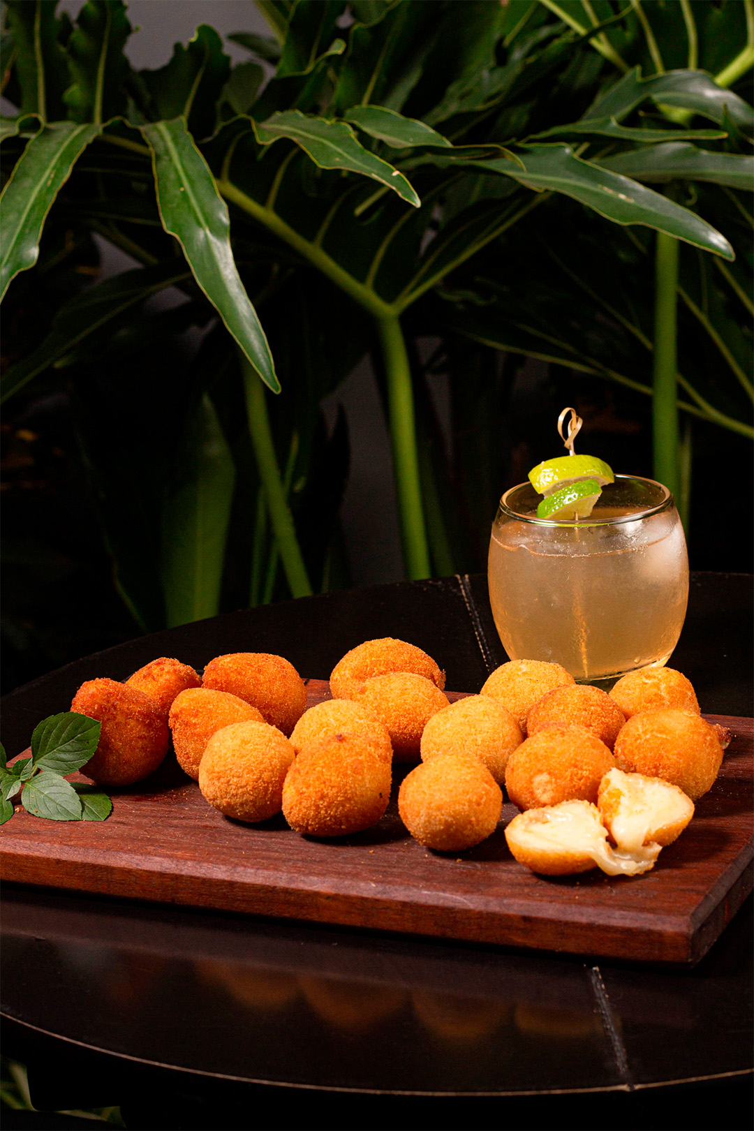 Tábua com bolinhas de queijo ao fundo copo com drink
