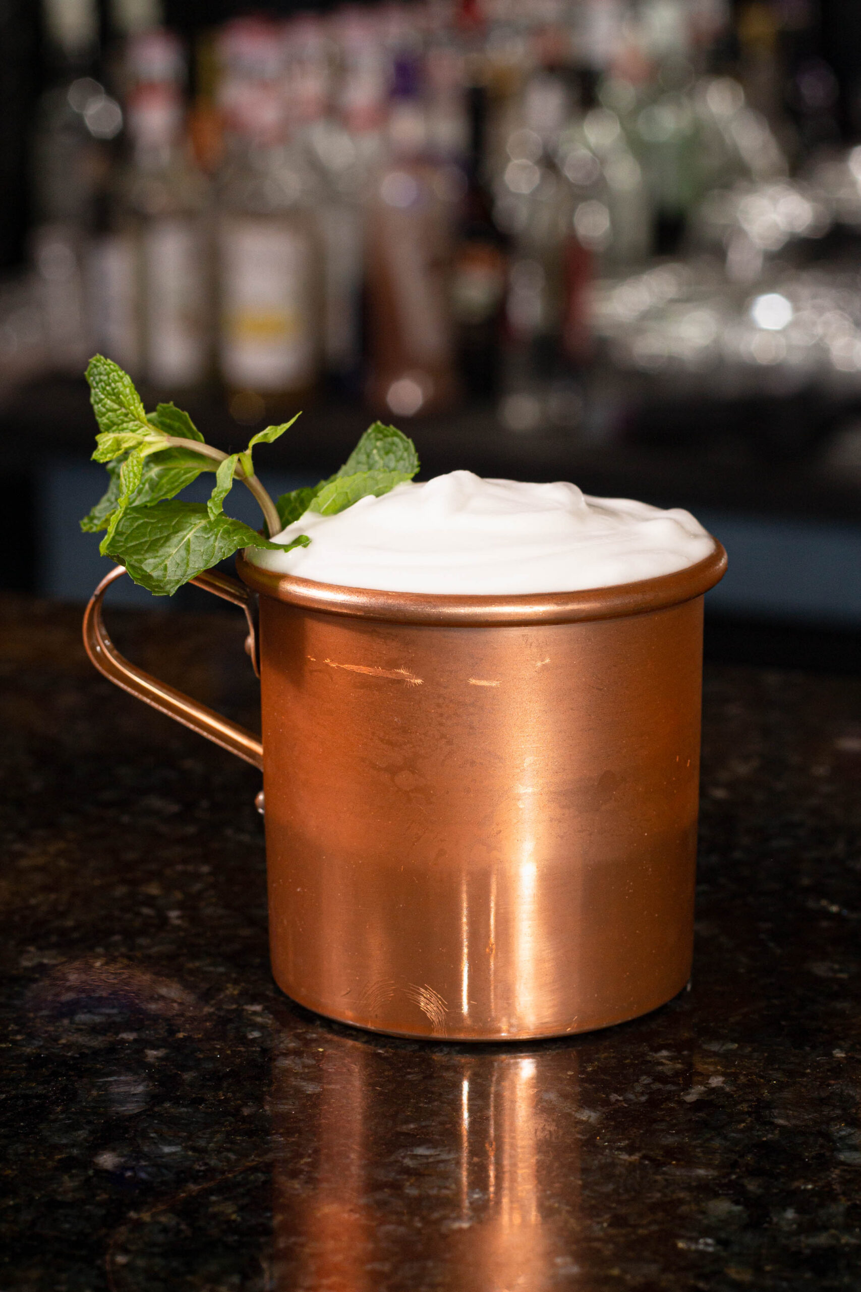copo de bronze com drink, espuma e hortelã.