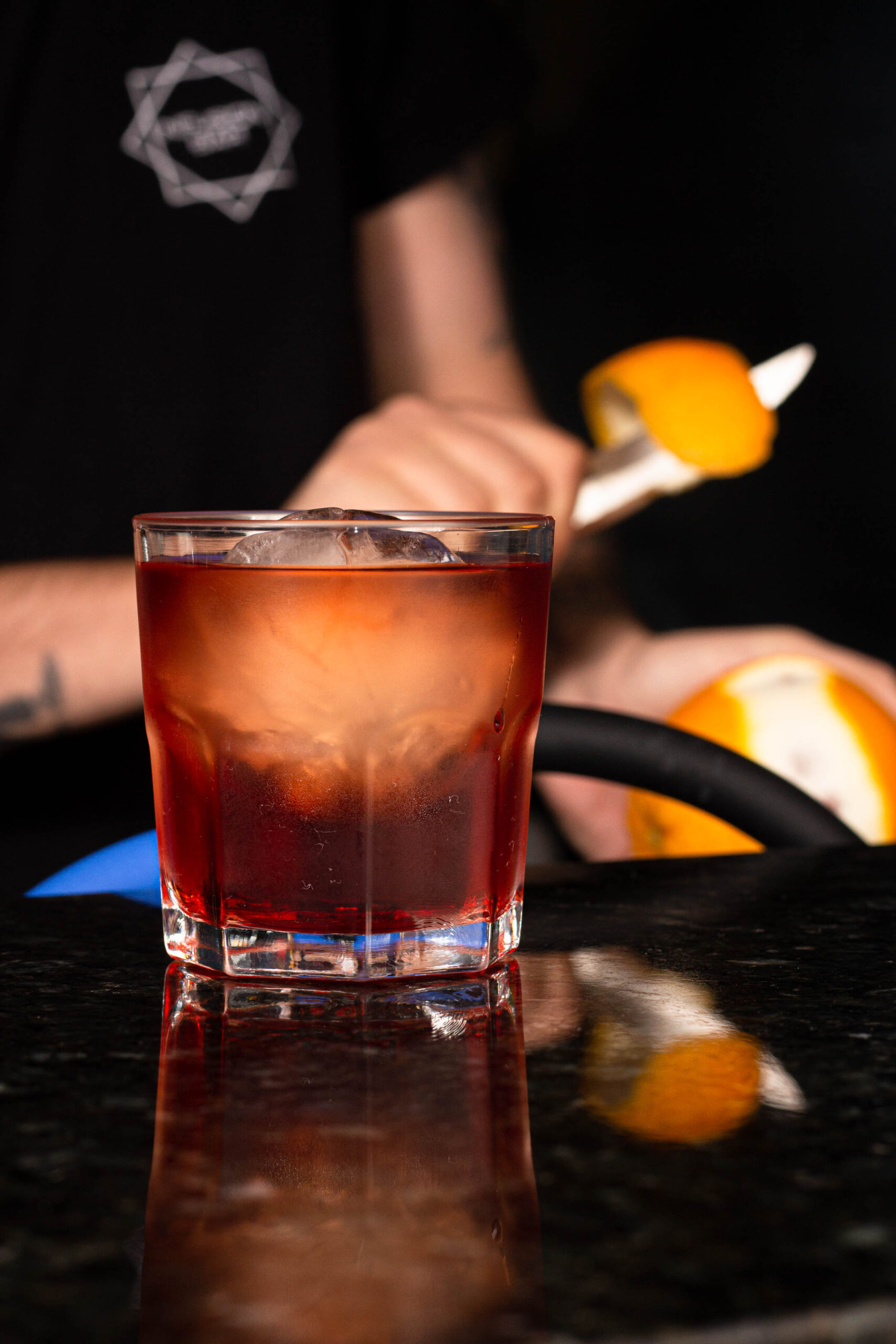 copo com drink, ao fundo uma pessoa descascando uma laranja