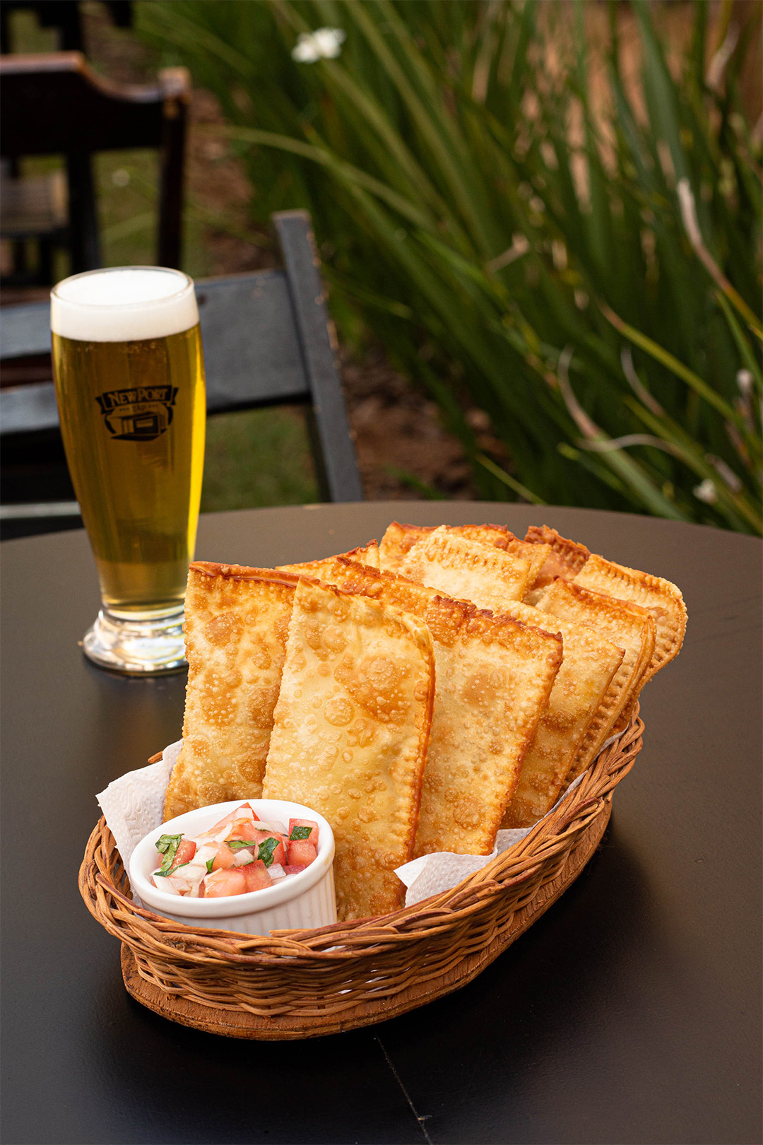 sexto com porção de pastéis e pote com vinagrete, atras um copo com cerveja.