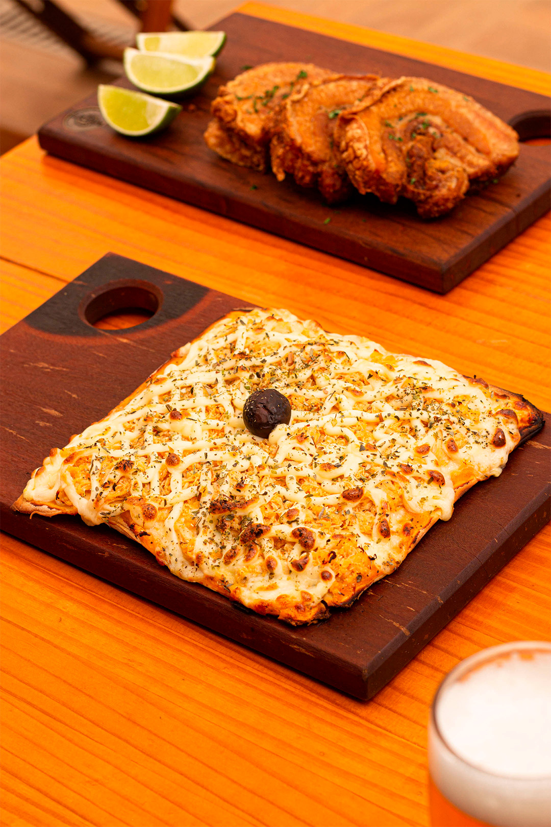 Tábua com pizza e ao fundo taboa com torresmo e limão