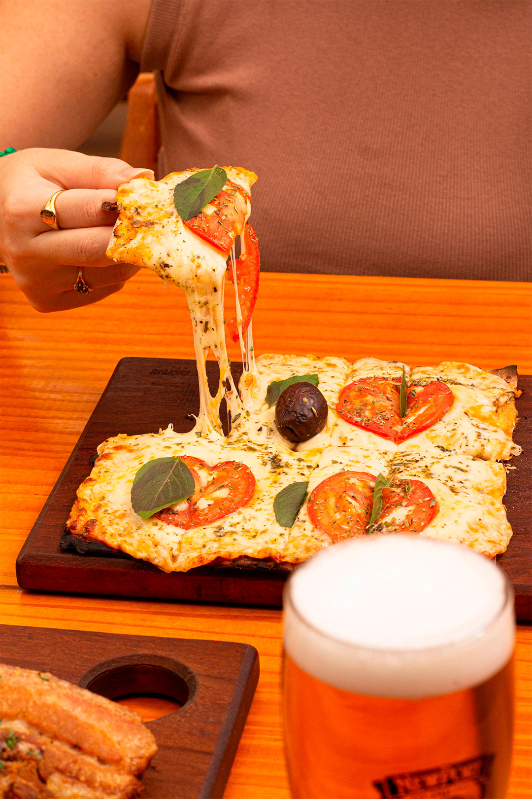 Tábua com pizza, mulher tirando um pedaço de pizza.