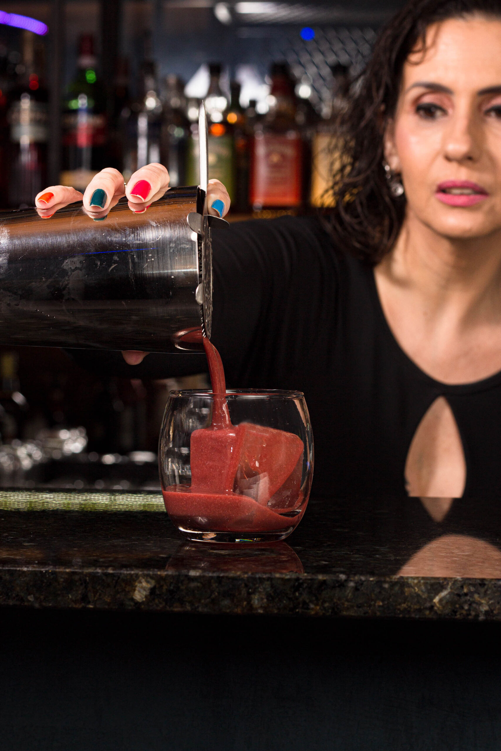 mulher despejando drink com uma coqueteleira no copo com gelo