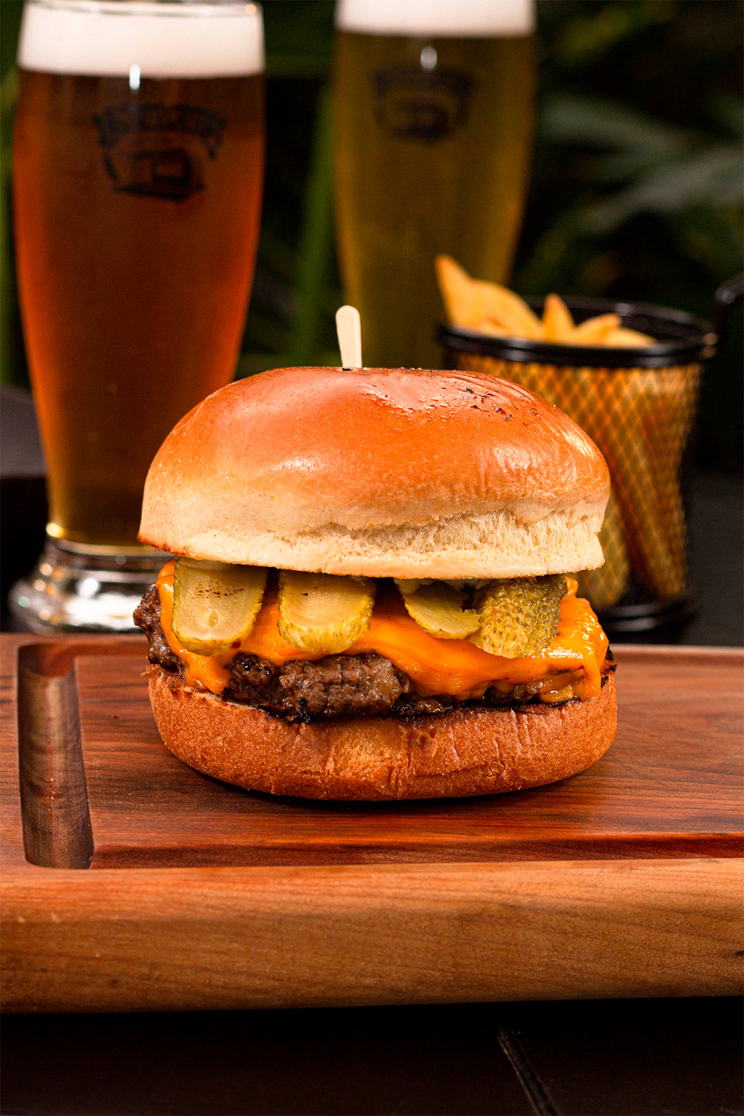 Tábua com hamburguer ao fundo copo com cerveja e batata frita.