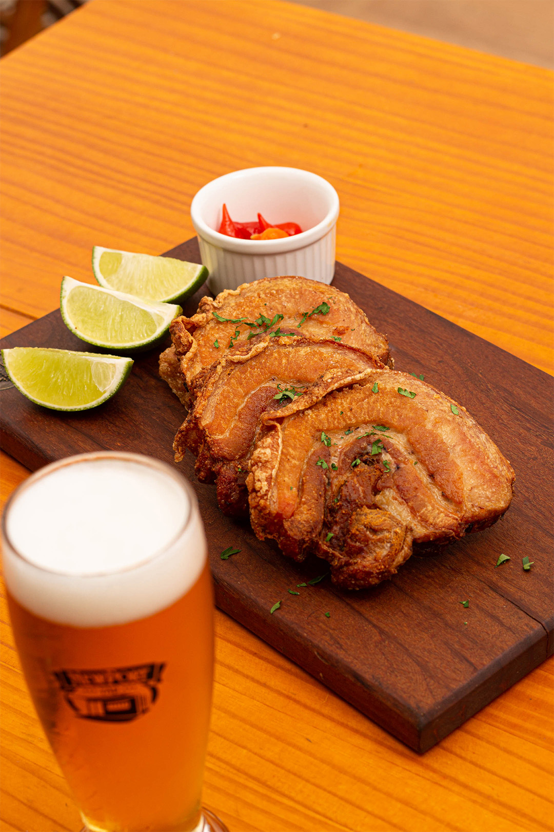 Tábua com torresmo, pimenta e limão. copo com cerveja